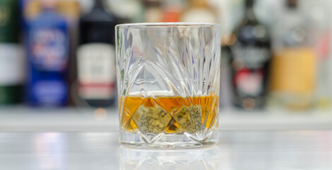 Old fashioned glass with scotch whisky and ice cubes on the bar