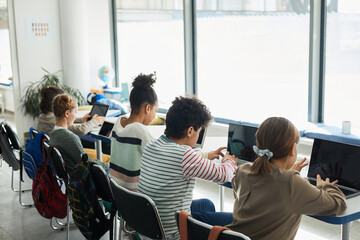 Back view at diverse group of children sitting in row at school classroom and using computers, copy space