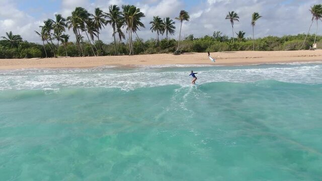 Aerial footage of a young woman surfing near the beach, light blue water