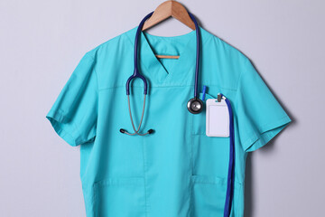 Turquoise doctor shirt with stethoscope, badge and pen hanging on light grey background