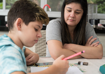 Mãe ajudando e orientando o filho estudante nas tarefas escolares dentro de casa. Dificuldades do ensino à distancia. 