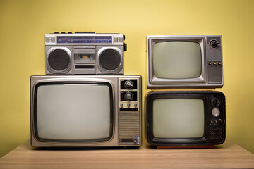 Retro old television with portable radio cassette recorder on wooden table in front of yellow wall background.
