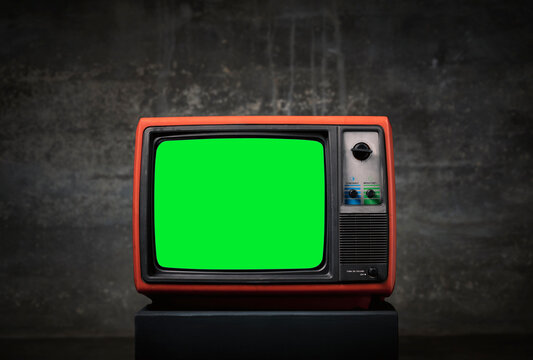 Retro old TV with green screen on wooden box in front of old wall background.