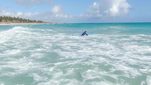 Drone view of a woman swimming on a surfboard in blue foamy water of the ocean