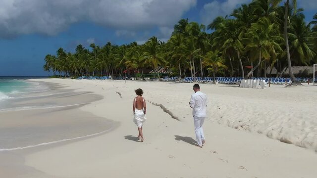 Couple in love is walking on a tropical beach, foamy blue ocean waves, vacation