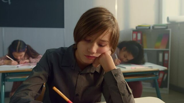 Tired schoolboy sitting in classroom. Cheerful boy boring during lesson