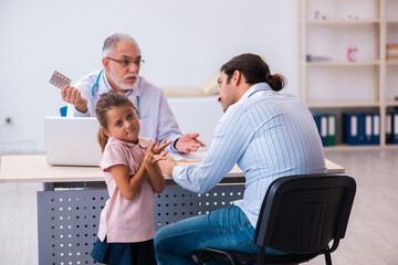 Obraz premium Small girl with her father visiting old male doctor