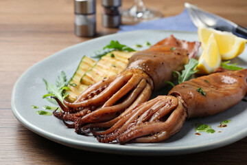 Delicious grilled squids served on wooden table, closeup