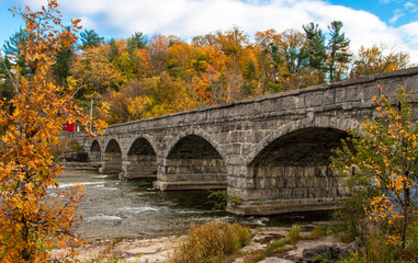 Fototapeta na wymiar Beautiful old stone stone bridge in autumn. The historic Pakenham five arched stone bridge spans the Mississippi River in Canada. Built ca. 1901, it's the only one of its kind outside of Russia.