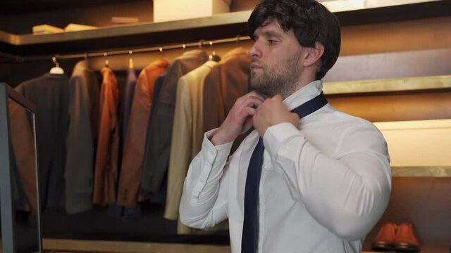 Man in a shirt gets dressed and adjusts a blue tie around his neck in the dressing room