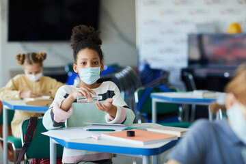 Portrait of young African-American girl sanitizing hands in school classroom, covid safety measures, copy space
