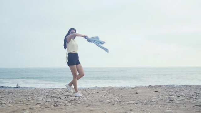 Mujer joven latina caminando feliz por la playa mientras tira su ropa por la playa durante un hermoso atardecer. Joven latina des estresándose mientras camina  
