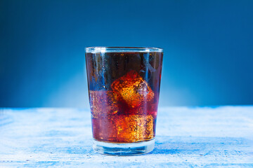 cola with ice in a glass bottle isolated on blue background.