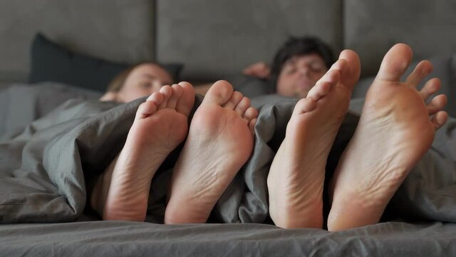 Loving joyful couple playing and dancing their feet under blanket while wake up in bed in the morning