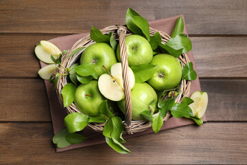 Fresh ripe green apples and leaves with wicker basket on wooden table, flat lay