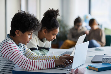 Fototapeta premium Side view portrait of two children using computers in modern school classroom, copy space