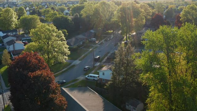 Rising aerial reveals American suburban neighborhood town. Homes under golden magic hour light in spring. Small town on outskirts of city.