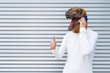 Happy man wearing dinosaur mask talking on phone showing thumb up