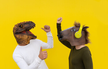 Funny couple of happy young man and woman with dinosaur and horse head mask dancing. Positive and...