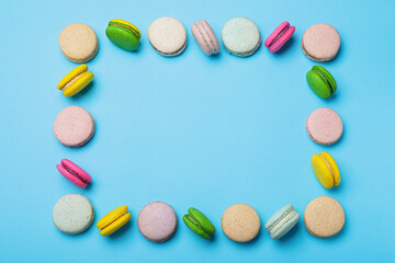 Fototapeta premium Frame made of delicious colorful macarons on light blue background, flat lay. Space for text