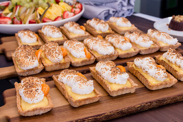 Tray of miniature lemon curd tarts on a dessert table with fruit salad in background