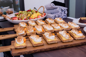 Tray of miniature lemon curd tarts on a dessert table with fruit salad in the background