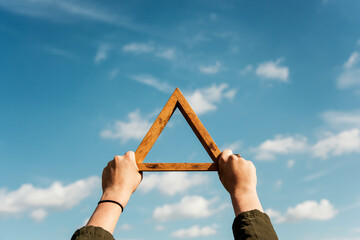 Hands holding wooden triangle frame up in a blue sky