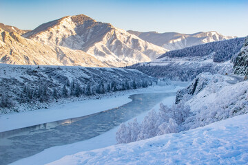 Fototapeta na wymiar winter, frosty, snowy landscape of the valley with a river, high mountain peaks with sharp bare stones, a winding highway and passing cars on it and clear sunny weather