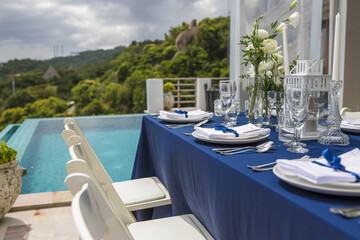 Blue and Silver Romantic Wedding Table Top Layout Table Spread no people catering, event, decor in a tropical location with the sea and clouds in the background