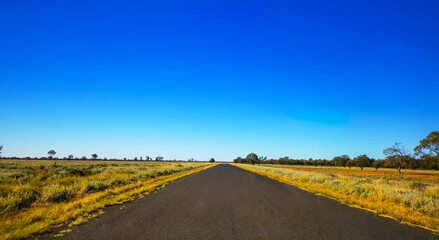 Fototapeta na wymiar View of straight country road in Australia with flat surrounding farmland and threatening storm clouds in the background.
