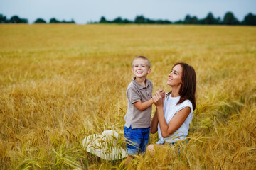 Happy family of a mother and a child in a summer wheat field. A young woman holds her son's hand.