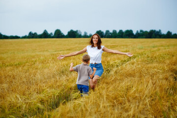 Naklejka na ściany i meble Happy family mother and son in a summer wheat field. The son runs to meet the mother, and she opens her arms for a hug