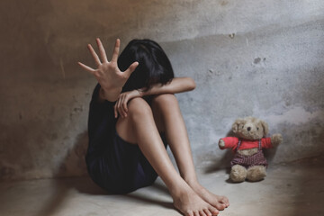 Little girl covered her face sitting alone on floor with her bear in dark room. concept for...