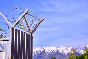 Fence with barbed wire on the background of snow-capped mountains and a blue sky with clouds; freedom concept