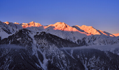 Soft morning sunlight on mountain ridges; rocky mountains covered with snow at sunrise