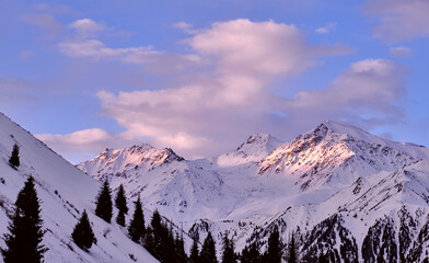 Soft morning sunlight on mountain ridges; rocky mountains covered with snow at sunrise