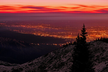 Aerial view of snow-capped mountains on the background of night city lights and sunset clouds