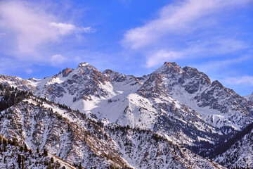Majestic rocky peaks with fir forest on the background of  blue sky with clouds  in the winter season
