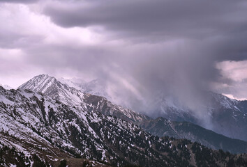 Spectacular snow clouds in a mountain gorge illuminated by the soft light of the morning sun; amazing natural phenomena, worsening weather, the approach of a snowstorm