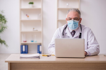 Old male doctor working in the clinic during pandemic