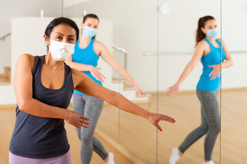 Hispanic woman in protective face mask learning dance moves during group training. New life reality...