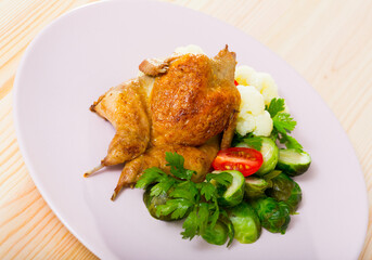 Delicious roasted small poultry with steamed vegetables on pink plate