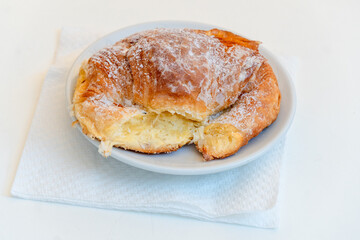Typical Italian breakfast croissant, or cornetto / cornetti, with  jam filling served on a small plate on white table.