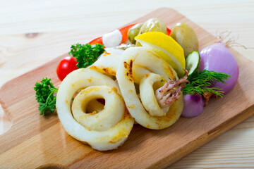 Baked squid rings with potatoes, fresh vegetables and herbs served on wooden board