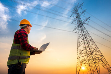 Picture of an electrical engineer using a notebook computer standing at a power station to see the...
