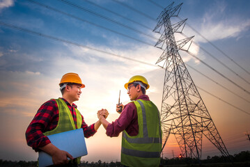 Two Asian men with electrical engineers standing at the power station standing in the air shaking hands agreeing to the production of electric power.