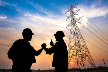 The silhouette of two electrical engineers standing at a power station standing in the air shaking...