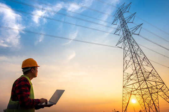 Picture of an electrical engineer using a notebook computer standing at a power station to see the planning work by producing electrical energy at high voltage electrodes
