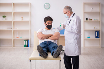 Fototapeta premium Young male patient visiting old doctor in vaccination concept