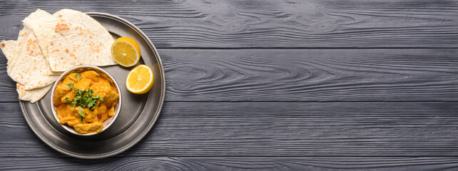 Bowl of tasty chicken tikka masala on wooden background with space for text
